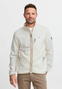 Veste en polaire blanche avec un col montant, dotée de deux poches zippées et d'une poche poitrine. Accentuée de garnitures et de quincaillerie contrastantes.
