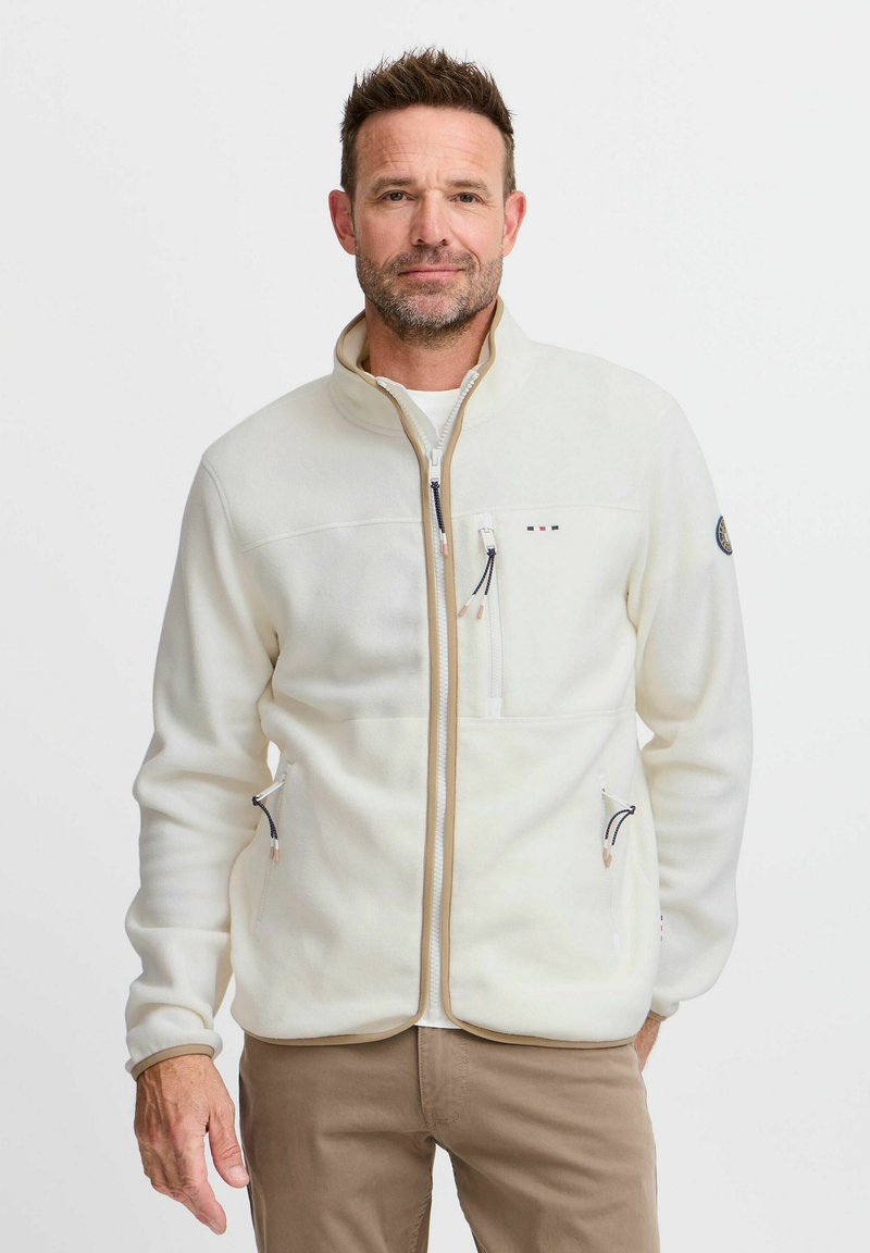 Veste en polaire blanche avec un col montant, dotée de deux poches zippées et d'une poche poitrine. Accentuée de garnitures et de quincaillerie contrastantes.