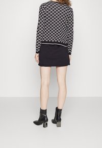 Maglione a maglia con motivo bianco e nero, con scollo rotondo, abbinato a una mini gonna nera e stivaletti con tacco quadrato.