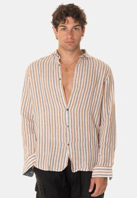 Camicia a maniche lunghe dal taglio morbido, bianca e con righe arancioni, dotata di un'apertura frontale, orlo curvo e texture morbida in lino.