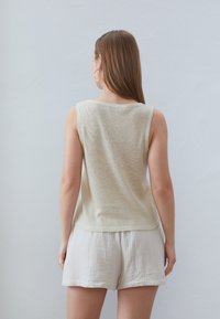 Top in maglina beige chiaro con un fit rilassato, caratterizzato da un collo rotondo e un tessuto testurizzato, abbinato a pantaloni corti grigi chiari.