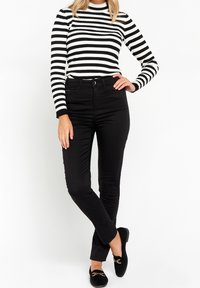 Svarta slim-fit byxor i kombination med en svart och vit randig långärmad topp. Platta svarta skor med en liten gulddetalj.