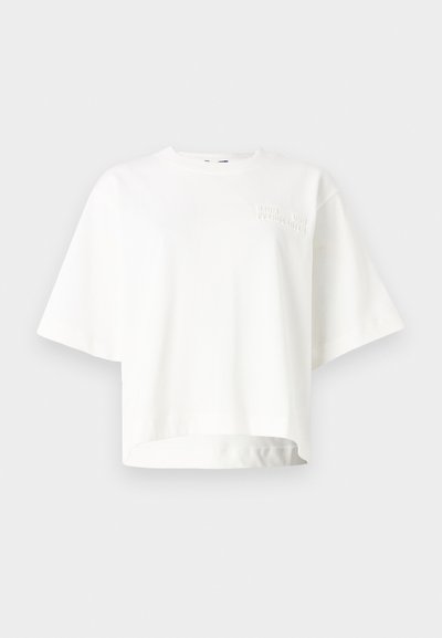 Camiseta corta de manga corta blanca, hecha de tela suave, con un sutil logo de la marca en relieve en la parte izquierda del pecho.