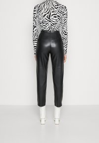 Svarta byxor i konstläder med hög midja, avsmalnande ben och slät yta, tillsammans med en topp i svart och vitt zebramönster.