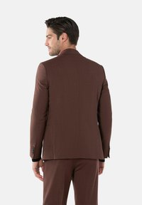 Brauner maßgeschneiderter Anzug aus strukturiertem Stoff, mit abgesetztem Revers und einem Ein-Knopf-Verschluss, versehen mit schwarzen Knopfakzenten.