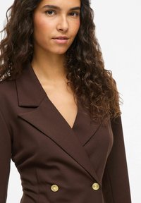 Rjavi dvoprsni blazer z zarezanimi reverji, gumbi v zlatem odtenku in oprijetim krojem. Gladek material z rahlim sijajem.