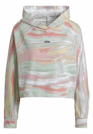 Personne portant un sweat à capuche pastel à motif marbré multicolore et un pantalon de jogging assorti avec des baskets blanches sur un fond uni.