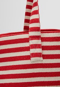 Sac en tissu rayé rouge et blanc avec des poignées robustes, doté d'une texture tissée et de coutures renforcées le long des bords.