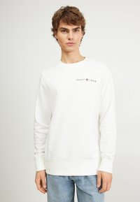 Hvid sweatshirt lavet af blødt stof, med rund hals og lange ærmer, samt et lille mørkt logo "GANT 1949" på brystet.