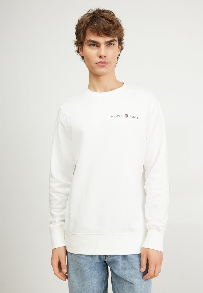 Hvid sweatshirt lavet af blødt stof, med rund hals og lange ærmer, samt et lille mørkt logo "GANT 1949" på brystet.