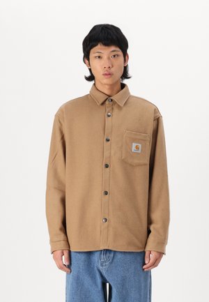 Brown flannel shirt with a button front, collar, and chest pocket; features silver buttons and a small logo patch on the pocket.