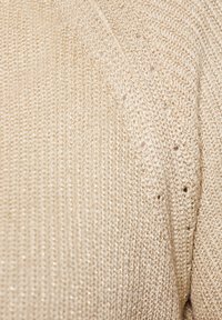Beżowy sweter dziergany o teksturowanym, błyszczącym wykończeniu. Posiada małe dziurki oraz miękką, lekką strukturę dla lepszej wentylacji.