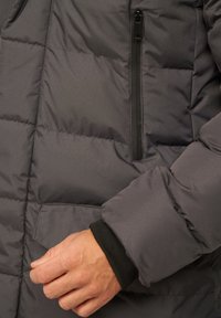 Graue Steppdaunenjacke mit einer Reißverschlusstasche, gesteppten Abschnitten und gerippten Bündchen. Glatte Textur und leichtes Material.