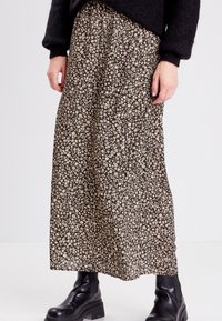 Maxikjol i svart tyg med ett litet beige blommönster. Flödande silhuett med resårmidja och samlade detaljer.