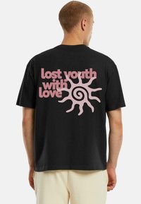 Černé bavlněné tričko s krátkými rukávy, na zadní straně s růžovým grafickým designem, který zní „ztracená mládež s láskou“ a s motivem slunce.
