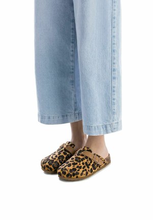 Zuecos de estampado de leopardo con una base y correa marrón, combinados con unos vaqueros de pierna ancha de color azul claro, que muestran un diseño de calzado casual.