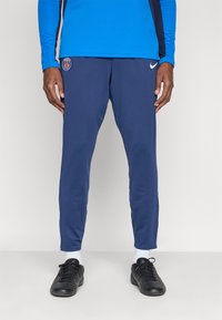 Tmavomodré športové nohavice s priliehavým strihom, s logom Paris Saint-Germain a emblémom Nike, vyrobené z elastického materiálu.