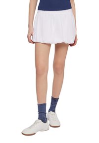 Gonna bianca con un design a pieghe morbido e svolazzante; abbinata a calze a coste blu navy e sneakers bianche. Tessuto liscio con una vita elasticizzata.