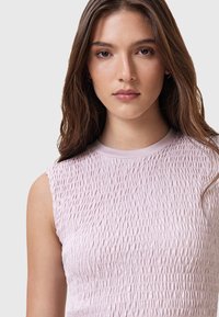 Ljusrosa ärmlös topp med en texturerad, samlad tygdesign och en rund halsringning som visar mjuka veck och en slät finish.