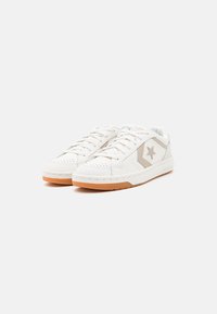 Baskets en cuir blanc avec des accents beige clair, arborant un logo en forme d'étoile, une pointe perforée et une semelle en caoutchouc gomme. Fermeture à lacets.