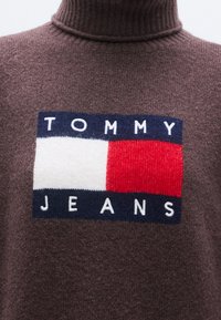 Καφέ πλεκτό πουλόβερ με ζιβάγκο, με ορθογώνιο λογότυπο "TOMMY JEANS" σε λευκό, κ�όκκινο και μπλε, με υφασμάτινη υφή σε απαλό φινίρισμα.