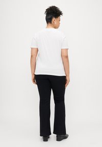 Fehér, rövidujjú póló, amely fekete trapéznadrággal van viselve. A pólón kerek nyakú, sima tapintású; a nadrágnak illeszkedő derékrésze van, és enyhe rugalmassággal bír.