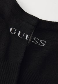 Suéter de punto negro de cuello alto con textura acanalada, con el logo "GUESS" en blanco en la parte frontal, posicionado ligeramente de forma asimétrica.