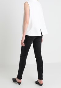 Vit ärmlös topp med en texturerad design, kombinerad med svarta skinny jeans som har ett subtilt mönster och fransade kanter, kompletterad med svarta ballerinaskor.