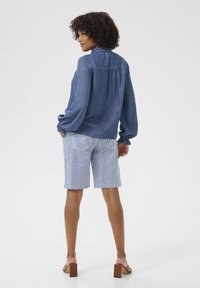 Jeanshemd met ballonmouwen, blauwe kleur, gecombineerd met gestreepte shorts. Bruine blokhakken sandalen; casual outfit met een relaxte pasvorm.