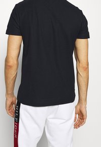Schwarzes T-Shirt mit kurzen Ärmeln und Rundhalsausschnitt. Glattes Baumwollmaterial, taillierte Passform, schlichte Rückseite ohne sichtbare Logos oder Muster.