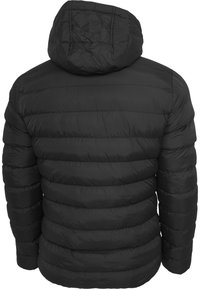 Veste matelassée noire avec un design matelassé horizontal, une capuche et une finition mate. Présente une coupe ajustée avec des sections légèrement rembourrées.