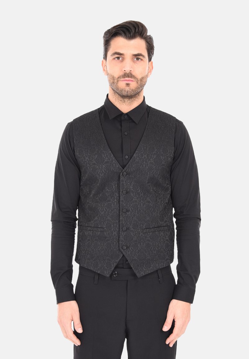 Gilet nero con un motivo testurizzato, dotato di colletto a punta, sei bottoni e tasche laterali. Indossato sopra una maglia nera aderente a maniche lunghe.
