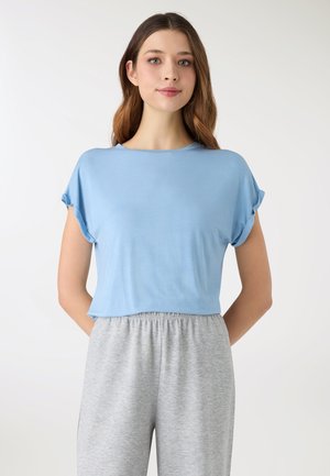 Top corto a maniche corte azzurro chiaro realizzato in tessuto morbido. Presenta una scollatura rotonda e polsini arrotolati, abbinato a pantaloni con fascia elastica grigia.