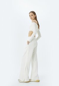 Witte off-shoulder crop top gecombineerd met high-waisted, brede pijpen met zijzakken en een ontspannen pasvorm. Glad textuur, minimalistisch ontwerp.