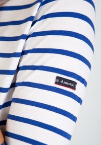 Camicia a maniche lunghe bianca con righe orizzontali blu, dotata di una piccola etichetta Armor Lux sulla manica. Tessuto di cotone morbido.