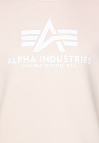Logo di Alpha Industries con una "A" stilizzata e tre linee orizzontali sopra il testo "Alpha Industries Knoxville, Tennessee, U.S.A." su tessuto chiaro.