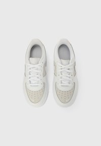 Λευκά και μπεζ αθλητικά παπούτ σια με επάνω μέρος από λείο δέρμα, διάτρητο μπροστινό μέρος και λευκά κορδόνια. Διαθέτουν διακριτικό λογότυπο στο πλάι.