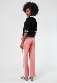 Top corto de punto negro con mangas de rayas, combinado con pantalones rosa de pierna ancha que cuentan con rayas laterales y aberturas. Zapatos plateados texturizados.