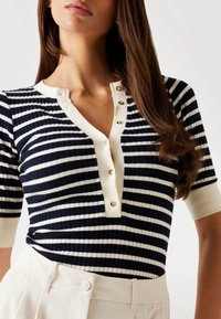 Navy and cream striped ribbed knit top with a V-neck, featuring a button placket with gold-tone buttons and elbow-length sleeves.