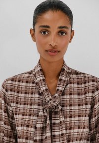 Bruine en beige geblokte blouse met een geknoopte halsband, uitgevoerd in een gladde stof en met een losse pasvorm.