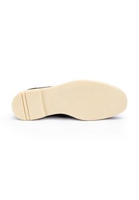 Semelle de chaussure noire avec une surface en caoutchouc crème texturée. Présente un design plat avec un léger talon et un nom de marque en relief.