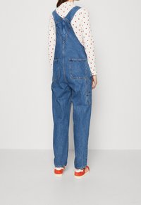 Salopette in denim con una vestibilità rilassata, dotata di due tasche posteriori e bretelle regolabili, abbinata a una camicia a maniche lunghe con motivi a cuore.