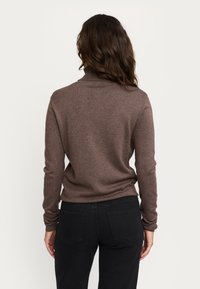 Pruun kaelusega turtleneck kampsun pikkade varrukatega, soonikuga krae ja tekstureeritud kudumise mustriga, millele on paaritatud mustad teksad, vaadet tagant.