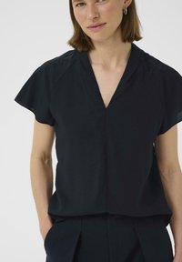 Top nero a maniche corte con scollatura a V, realizzato in un tessuto testurizzato. Presenta una vestibilità morbida e dettagli sottili sulle cuciture delle spalle.