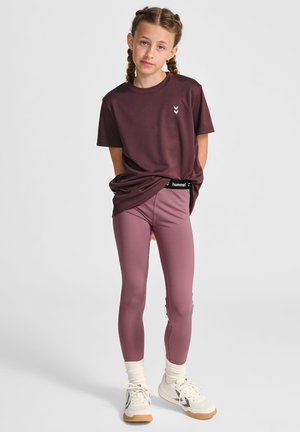 T-shirt bordeaux, col rond, avec logo blanc. Leggings roses, taille haute, texture lisse. Chaussures de sport blanches avec semelles en caoutchouc et chaussettes de cheville.
