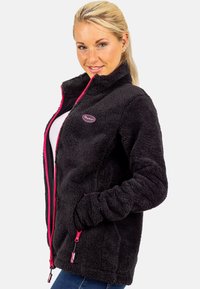 Schwarze Fleecejacke mit weicher Textur, verfügt über pinkfarbene Reißverschlussakzente, hohen Kragen und seitliche Taschen. Logopatch im Brustbereich.
