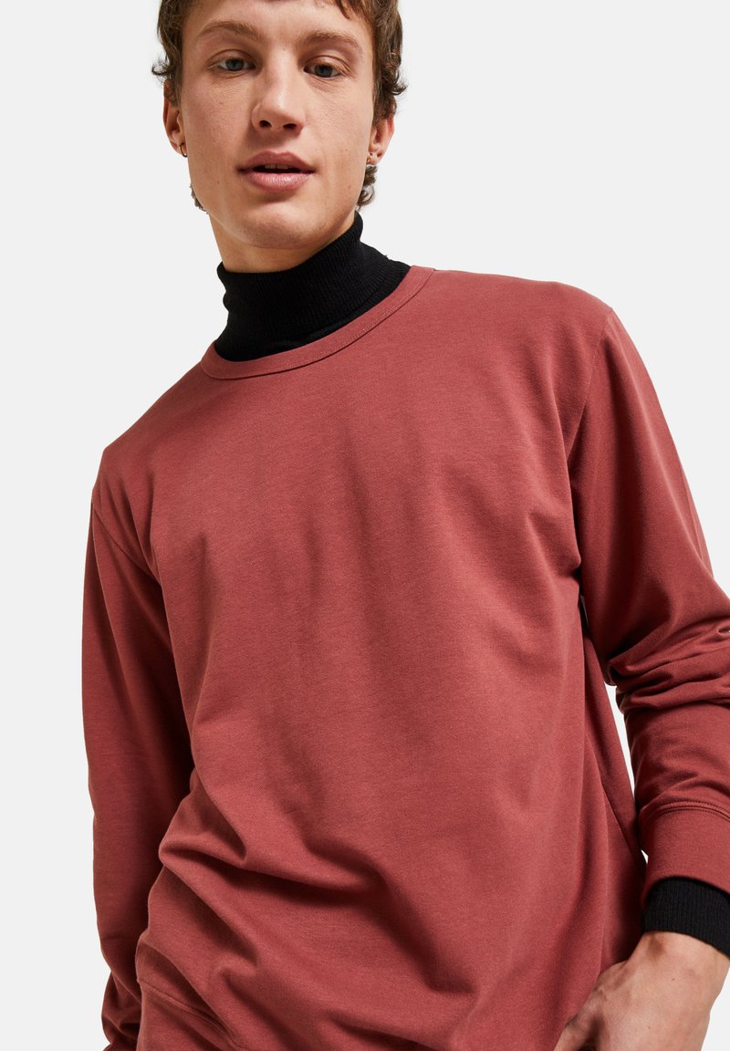 T-shirt à manches longues de couleur rose avec un col rond, fabriqué en tissu doux, doté d'une couche de col montant noir en dessous.