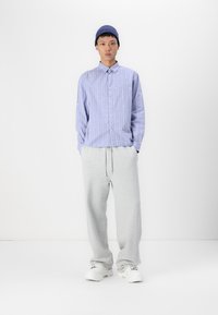Light blue vertical striped shirt with white accents, paired with gray sweatpants. Model wears a blue ribbed beanie and white sneakers.