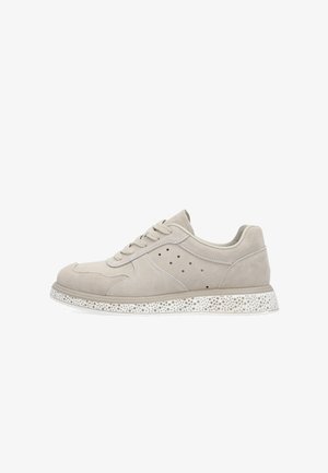 Licht beige suède sneaker met vetersluiting, geperforeerde zijpanelen en een witte rubberen zool met een patroon van kleine gaatjes.