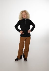 Schwarzer Quarter-Zip-Pullover, braune weite Hose und schwarze Stiefel mit roten Akzenten. Glattes Material, lockere Passform und minimalistisches Design.